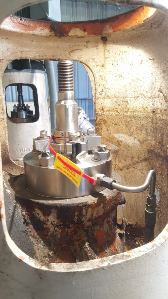 Stainless steel shaft seal with a caution tag, seen through an opening in a pump stand