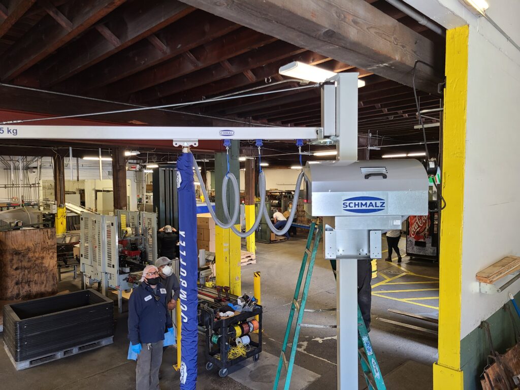Workers beside a vacuum tube lifter on a white jib arm in a warehouse
