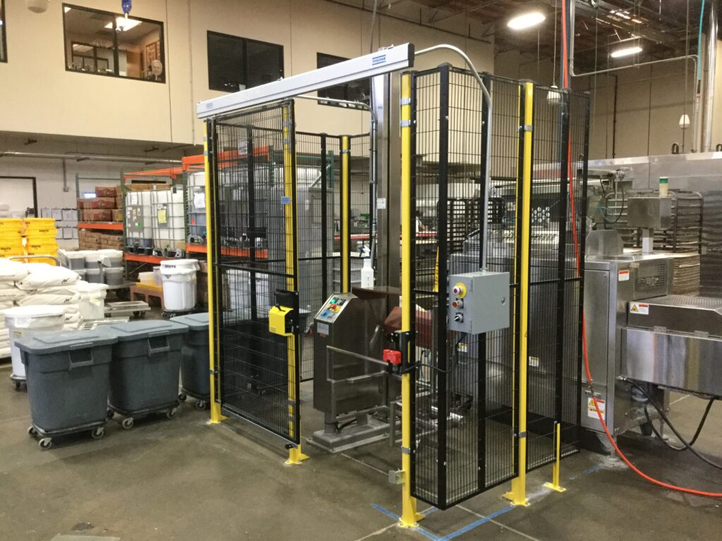 Wire-mesh safety enclosure with yellow posts around a machine in a production plant