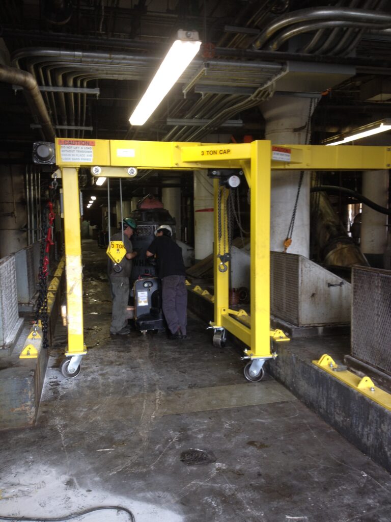 Two workers under a yellow 3-ton portable gantry crane in a plant