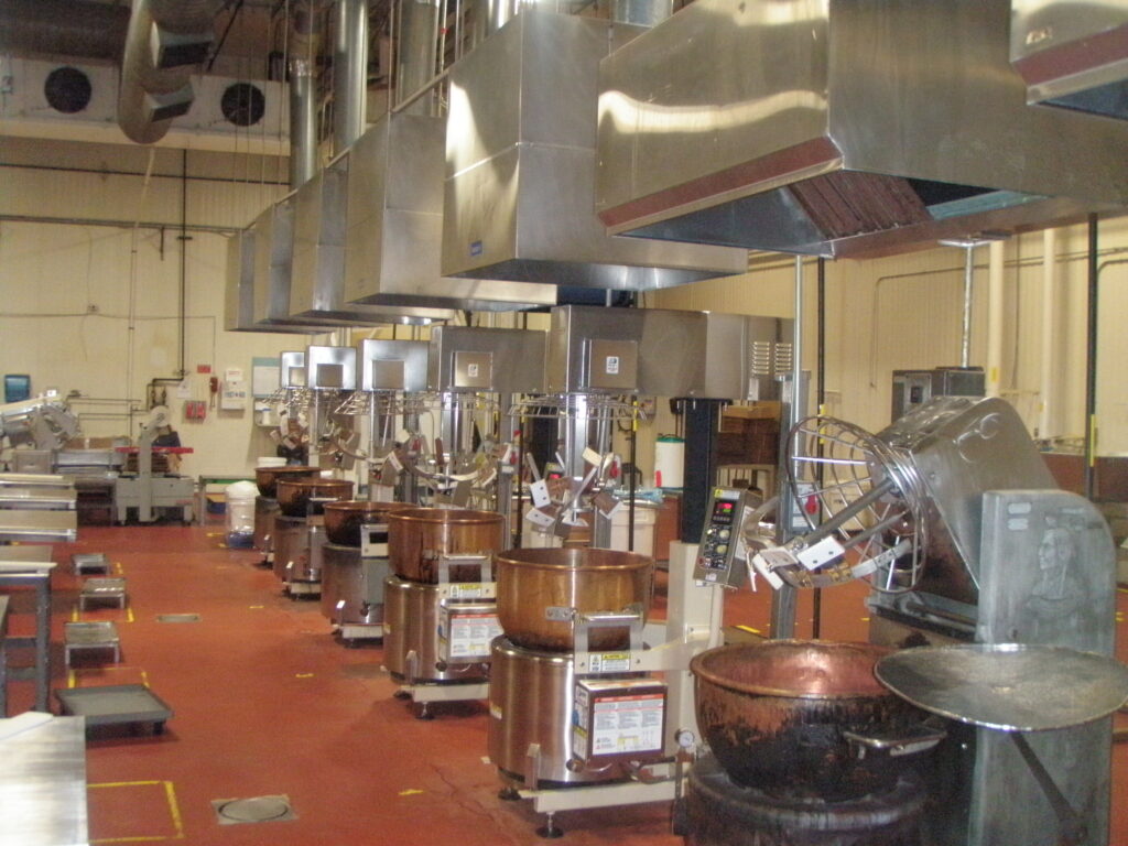 Row of copper cooking kettles with mixers under stainless steel hoods in a production kitchen