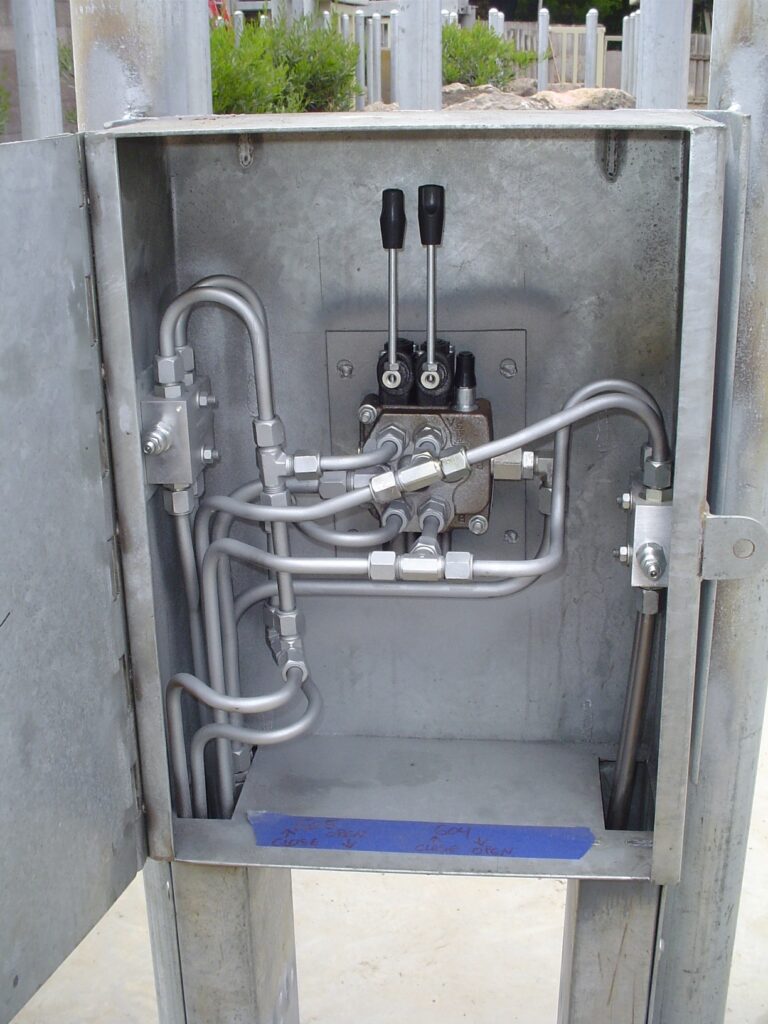 Two-lever hydraulic control valve and tubing inside an open galvanized steel cabinet
