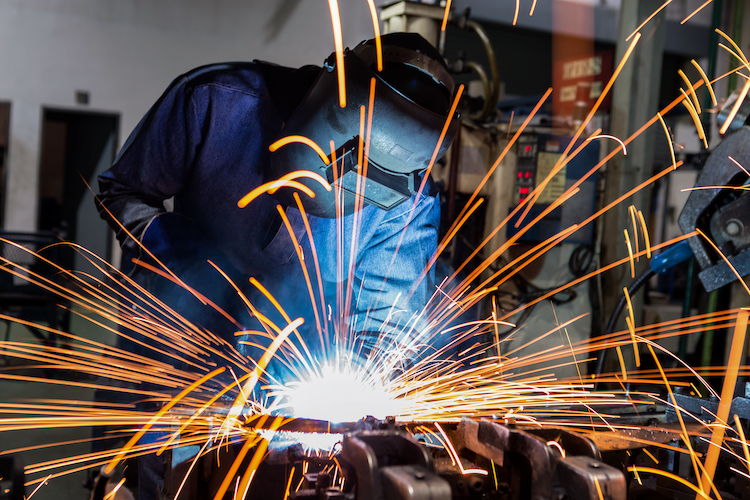 Welder welding in blue suit with sparks | Mathews Mechanical